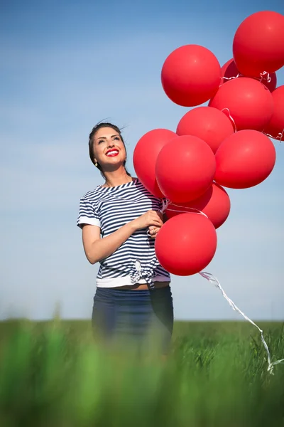 Mujer joven feliz con un globo rojo en un prado verde —  Fotos de Stock