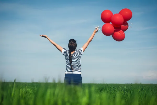 Happy young woman with a red balloon on a green meadow — Stock Photo, Image