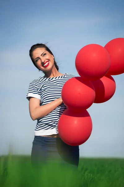Šťastná mladá žena s červeným balónkem na zelené louce — Stock fotografie