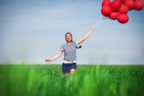 Happy young woman with a red balloon on a green meadow — Stock Photo, Image