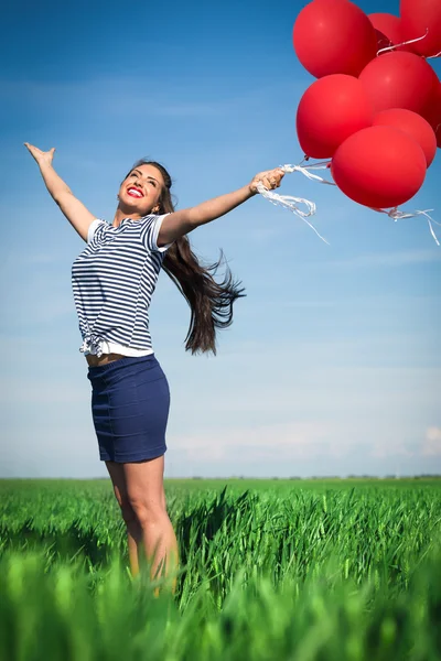 在一片绿色的草地上一个红气球的幸福年轻女人 — 图库照片