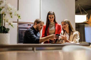 Modern bir galeride veya ofiste tasarım seçeneklerini tartışan üç genç profesyonel