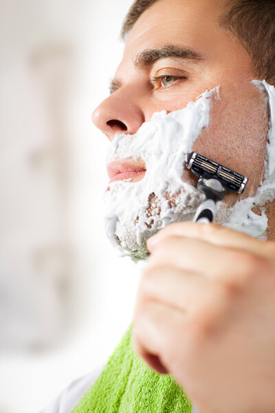 Handsome young man is shaving his face