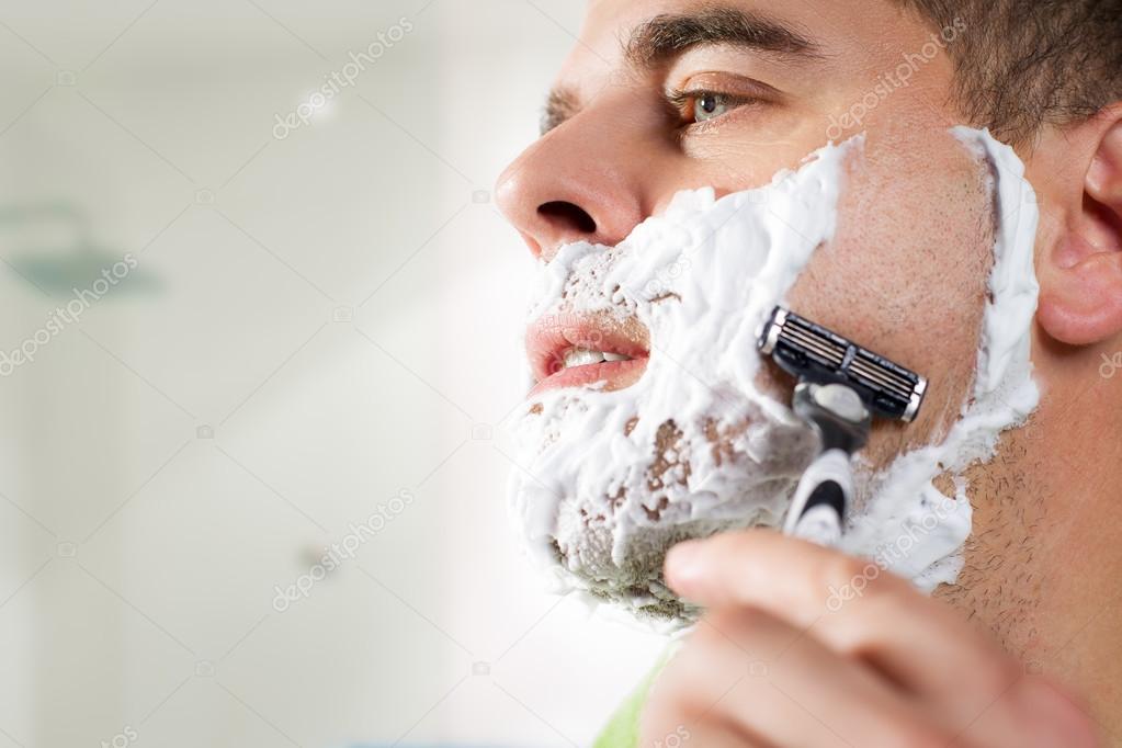 Handsome young man is shaving his face