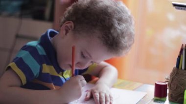 Küçük çocuk evde bir masada resim çiziyor. Çocuk yaratıcılıkla meşgul, evde çalışıyor, video çekiyor.