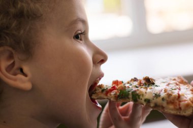 Pizza yiyen çocuk, yakın plan, yan görüş. Elinde bir dilim pizza. Bir kafede öğle yemeği, Lafstyle.