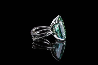 Siyah zemin üzerinde büyük kare şeklinde yeşil mücevher olan gümüş bir yüzük.