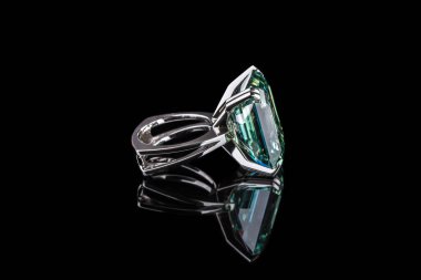 Siyah zemin üzerinde büyük kare şeklinde yeşil mücevher olan gümüş bir yüzük.