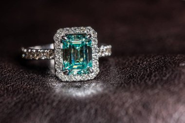 Büyük yeşil mücevher ve küçük elmaslarla dokulu deri üzerinde duran gümüş bir yüzük.