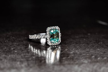 Büyük yeşil taşlı gümüş yüzük ve dokulu arka planda duran küçük elmaslar.