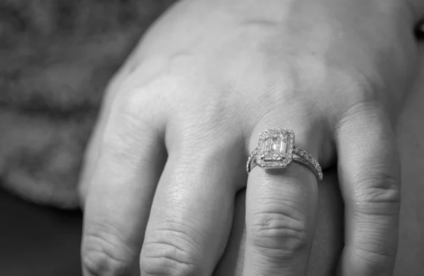 Black and white photo of hand with silver ring with big gem and small diamonds on it