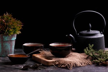 Yeşil yapraklı çay seremonisi ve ahşap masada çaydanlık.