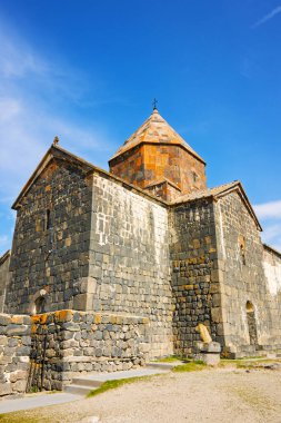 Bir Sevan Manastırı Sevanavank 'ın tepesinde çan kulesi ve haçı var. Binanın etrafı taştan bir duvarla çevrili ve ona doğru uzanan taş bir merdiveni var. Gökyüzü açık ve mavi