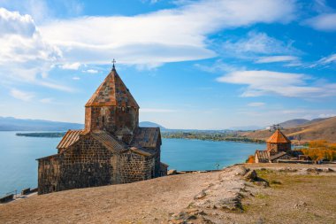 Bir Sevan Manastırı Sevanavank kilisesi bir tepenin üzerinde su birikintisine bakıyor. Gökyüzü açık ve güneş parlıyor.