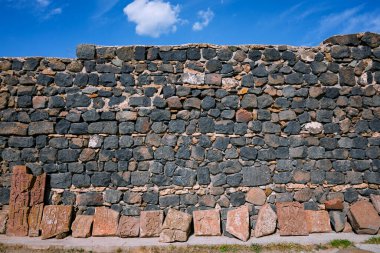 Arkasında mavi bir gökyüzü olan taş bloklardan yapılmış bir duvar. Duvar çok yüksek ve blokların arasında çok yer var.