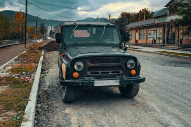 Siyah bir SSCB cipi yolun kenarına park edilmiş. Cip kirli ve üzerinde birkaç çizik var. Yol boş ve görünürde başka araç yok. Sahne yalnızlık hissi veriyor.