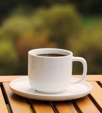 Kahverengi sıvılı beyaz bir kahve fincanı ahşap bir masanın üzerinde duruyor. Kupa beyaz bir fincan tabağının üzerine konur, o da masanın üzerindedir. Rahatlama ve rahatlama kavramı