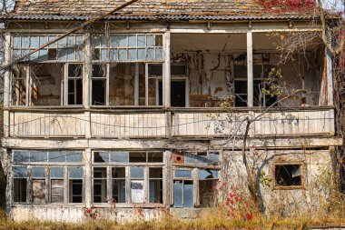 Kırık camları ve sarmaşıkları olan harap, terk edilmiş bir ev. Ev bakımsız görünüyor. Çürüme ve terk edilme hissi var.