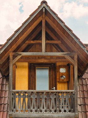 Duvarında saat olan ahşap bir balkon. Balkon açık ve parmaklıkları var.