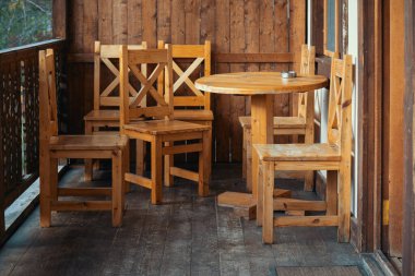 Yuvarlak masalı ahşap bir teras seti ve altı tahta sandalye. Sandalyeler masanın etrafına dizildi ve masanın üzerinde bir fincan var. Sandalyeler gibi rahatlama ve rahatlama kavramı.