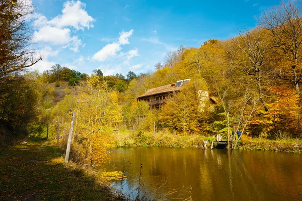 Bir ev bir göl kenarındaki yamaçta bulunur. Ev ağaçlarla çevrili ve göl sakin ve huzurlu. Gökyüzü açık ve güneş ışıl ışıl parlıyor. Sahne huzurlu ve resimli.