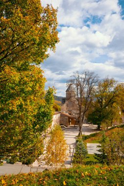 Arka planda bir kilisenin olduğu güzel bir sonbahar günü. Ağaçlar yapraklarla dolu ve gökyüzü bulutlu.