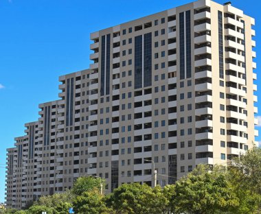 Önünde bir sürü penceresi ve yeşil ağacı olan büyük, çok katlı bir bina. Bina çok yüksek ve bir sürü penceresi var. Modern ve şık bir görünüme sahip.