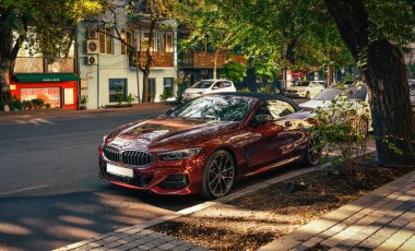 Erivan, Ermenistan 10.16.2025. Kırmızı bir BMW bir binanın önündeki caddenin kenarına park edilmiştir. Araba bir ağacın yanındaki otoparkta park halinde.