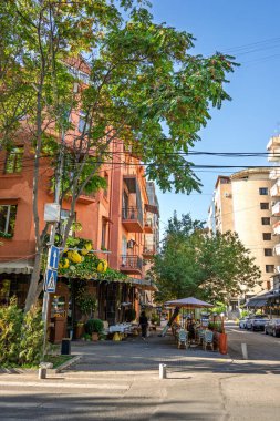 Erivan, Ermenistan 10.16.2025. Arka planda bir bina ve ön planda bir ağaç olan bir sokak sahnesi. Sokak masa ve sandalyelerle dolu ve dışarıda birkaç kişi oturuyor. Atmosfer rahat.