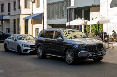 Erivan, Ermenistan 10.16.2025. İki lüks araba bir caddede yan yana park edilir. Arabalar siyah ve gümüş renginde ve tenteli bir binanın önünde park halindeler.