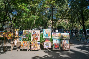 Erivan, Ermenistan 10.16.2025. Bir grup resim bir parktaki kaldırımda sergileniyor. Tablolar çeşitli boyut ve stillerde ve sırayla dizilmiş.