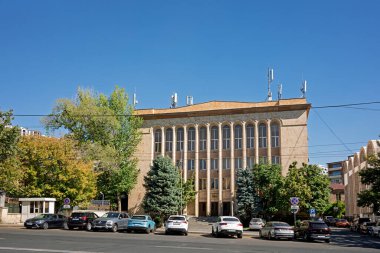 Erivan, Ermenistan 10.16.2025. Önünde bir sürü pencere ve bir ağaç olan büyük bir bina. Cadde park halindeki arabalarla dolu.