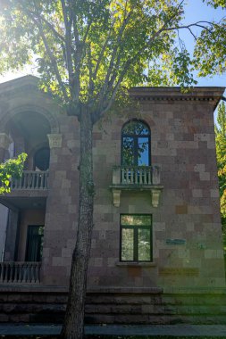 Erivan, Ermenistan 10.16.2025. Önünde ağaç olan büyük bir tuğla bina. Binanın balkonunda bir tabela var.