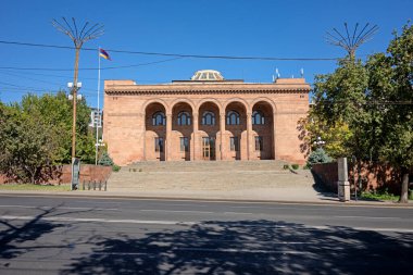 Erivan, Ermenistan 10.16.2025. Kemerli pencereleri ve kırmızı çatısı olan büyük bir bina. Bina ağaçlarla çevrili ve büyük bir avlusu var.