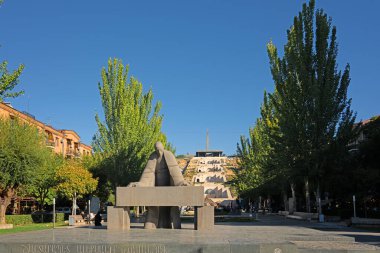 Erivan, Ermenistan 10.16.2025. Arkasında mavi gökyüzü olan bir binanın önünde büyük bir Tamanyan heykeli duruyor. Heykel ağaçlar ve bir çeşme ile çevrilidir. Huzurlu ve huzurlu bir sahne.