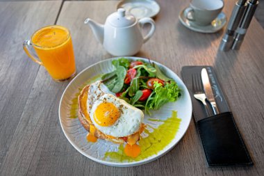 Üstünde yumurta ve salata olan bir tabak yemek istiyorum. Tabak bir bardak meyve suyu ve çaydanlıkla birlikte bir masanın üzerinde. Sahne rahat ve rahat.