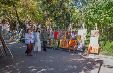 Erivan, Ermenistan 10.16.2025. Bir grup insan bir resim sergisinin önünden geçiyor. Tablolar sehpalarda sergileniyor ve çeşitli boyutlarda ve stillerde. Sahne, boş zamanlardan ve sanatın takdir edilmesidir.