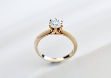 Ortasında küçük bir elmas olan altın ve beyaz bir elmas yüzük. Yüzük altın bir bantta ve beyaz bir yüzeye yerleştirilmiştir.