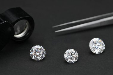 Siyah bir arkaplanda üç elmas sergileniyor. Elmasların hepsi aynı boyda ve şekilli, ve hepsi bir yüzüğe yerleştirilmiş. Yüzük masaya konur.