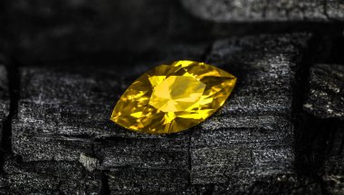 Siyah bir yüzeyde sarı bir taş var. Taş parlak ve sarı bir tonu var.