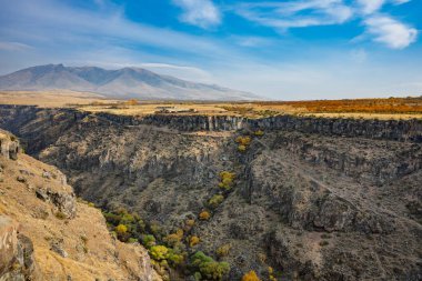 İçinden nehir akan bir dağ sırası. Dağlar ağaçlarla kaplı ve nehir kahverengi.