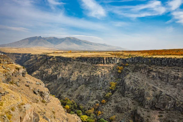 İçinden nehir akan bir dağ sırası. Gökyüzü mavi ve güneş parlıyor.