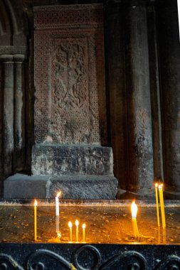 Taş bir sütunun önündeki masada yanan bir mum var. Sütun bir haç ve diğer sembollerle süslenmiş. Mumlar yanar ve sıraya dizilir, sıcak ve davetkar bir atmosfer yaratır.