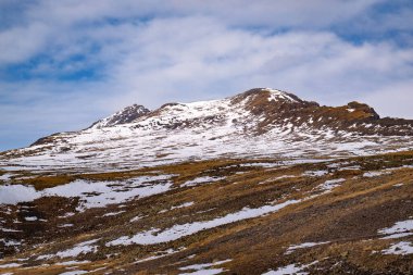 Kar ve kayalarla kaplı bir dağ. Gökyüzü mavi ve kar beyaz. Dağ çok yüksek ve kar onu kaplıyor.