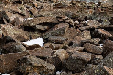 Üstünde kar olan bir kaya yığını. Kayalar büyük ve pürüzlüdür ve tepesindeki kar manzaraya derinlik ve kontrastlık katar. Görüntü, sertlik ve doğal güzelliği çağrıştırıyor.