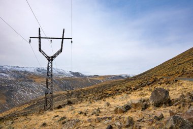 Arka planda bulutlu bir gökyüzü olan bir tepenin üzerinde bir elektrik hattı kulesi var. İzolasyon ve yalnızlık kavramı. Elektrik hattı kulesi çorak yamaçta tek başına duruyor.