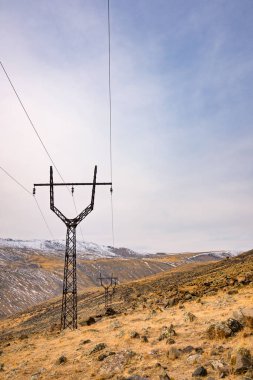 Bir elektrik hattı kulesi açık mavi gökyüzü olan bir yamaçta. Gökyüzü beyaz bulutlarla dolu.