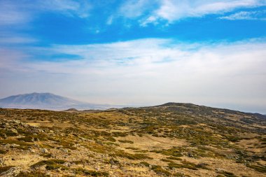 Bir dağ, çok kuru ve çorak bir arazinin arka planındadır. Gökyüzü açık ve mavi, görünürde bulut yok.