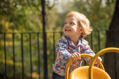 Küçük bir kız sarı bir salıncakta oturuyor. Gülümsüyor ve eğleniyor.