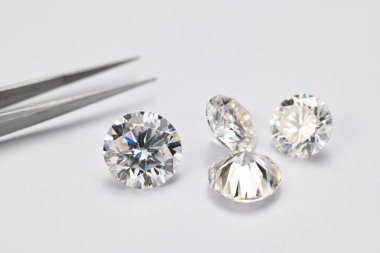 Beyaz arka planda dört beyaz elmas sergileniyor. Elmasların hepsi farklı boyutlarda ve bir yüzüğe yerleştirilmiş. Yüzük gümüş ve siyah olan bir çift maşa içinde tutulur.